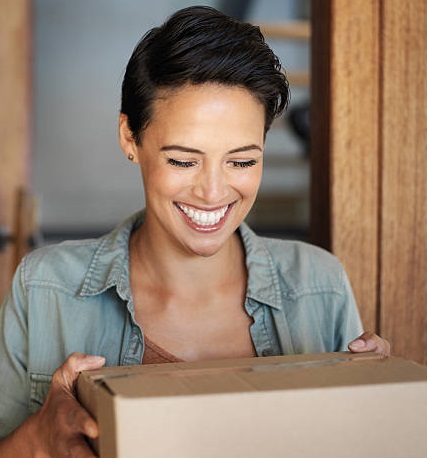 A girl receiving a parcel from the courier. She is smiling.